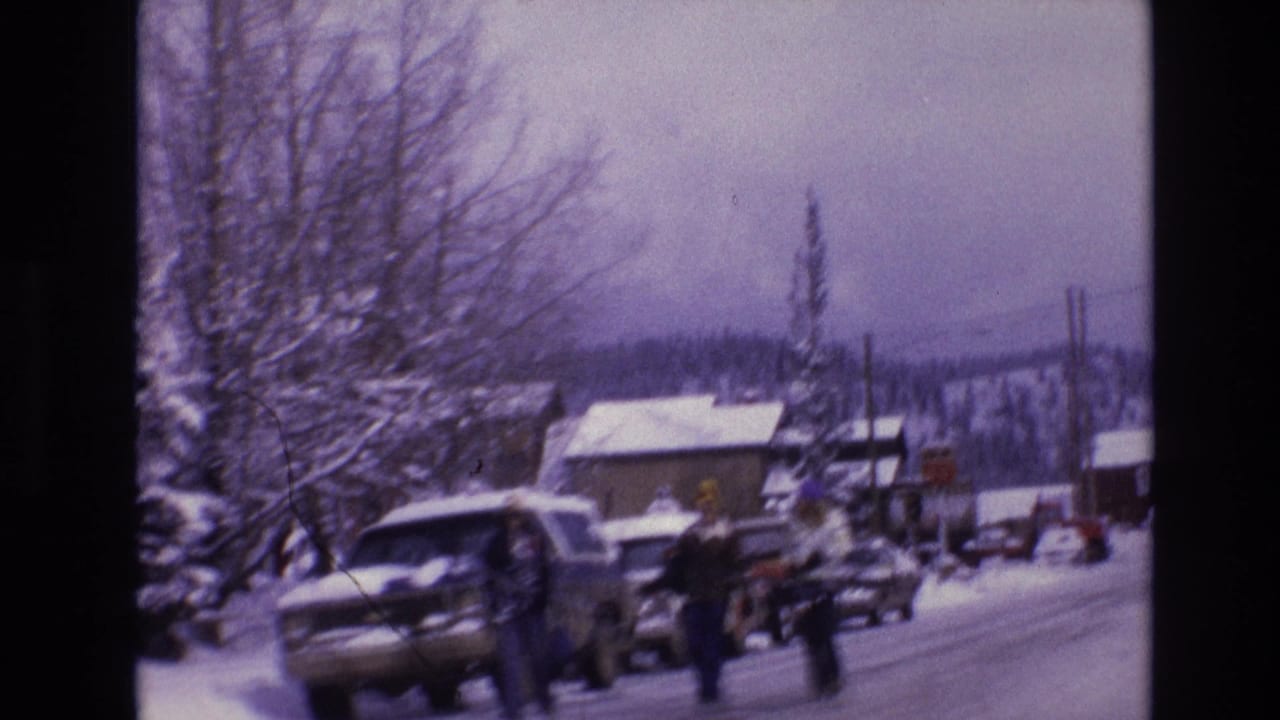 1974 Vail, Colorado street view with snow-covered cars, pedestrians in winter clothing, bare trees, and low buildings along the road.