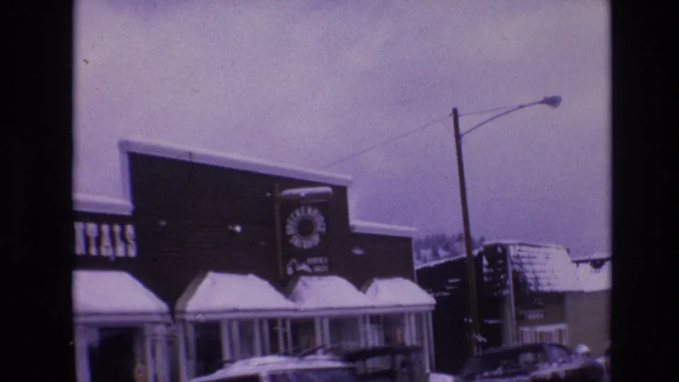 1974 Vail, Colorado storefront view showing a snow-covered building with a rentals sign, porch columns, a streetlight, and a parked car nearby.
