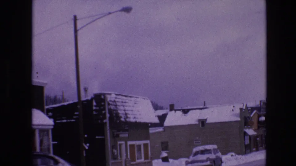 1974 Vail, Colorado commercial street view with snow-covered rooftops, storefronts, a streetlight, a parked car, and winter sky.