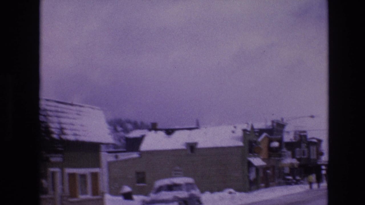 A snow-covered Vail, Colorado street scene from 1974 shows low commercial buildings, parked cars, winter rooftops, and visible 8mm frame edges.