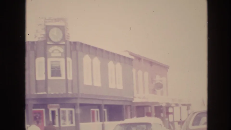 Faded 8mm frame from Vail, Colorado showing a two-story street building with a clock-like facade detail, arched upper windows, and parked cars in the foreground.