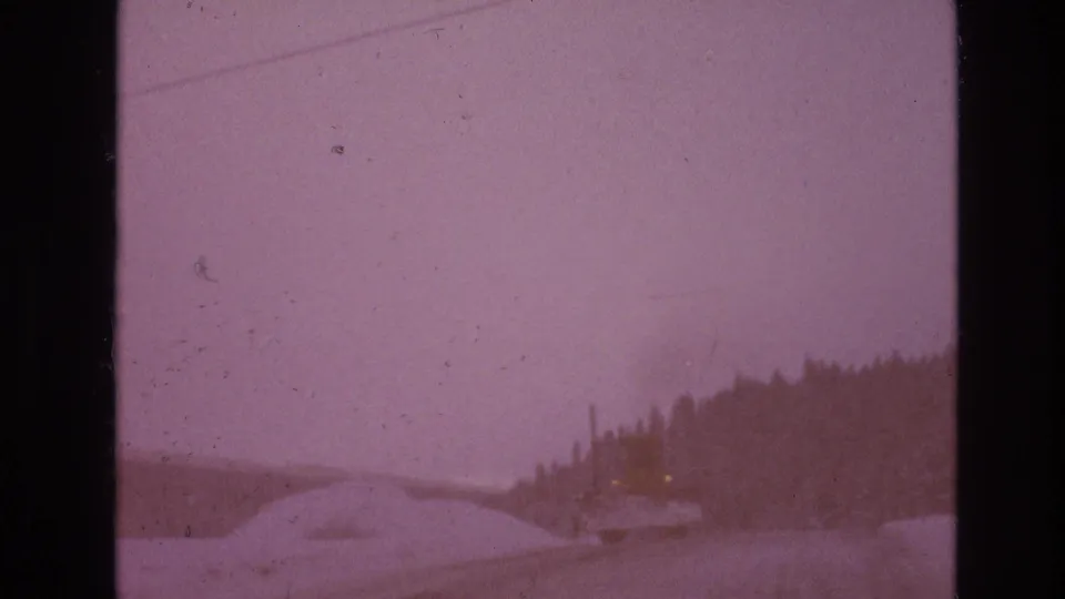 Pink-purple shifted 8mm frame of a snowy road near Vail, Colorado, with a forested hillside, utility pole, snowbanks, and faint lights at the roadside.