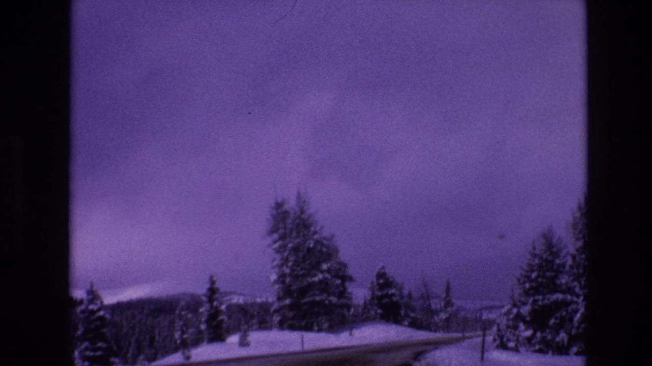 1974 Vail, Colorado frame with a curving snow-lined road, dark evergreen trees, distant mountain ridge, and visible 8mm color shift.