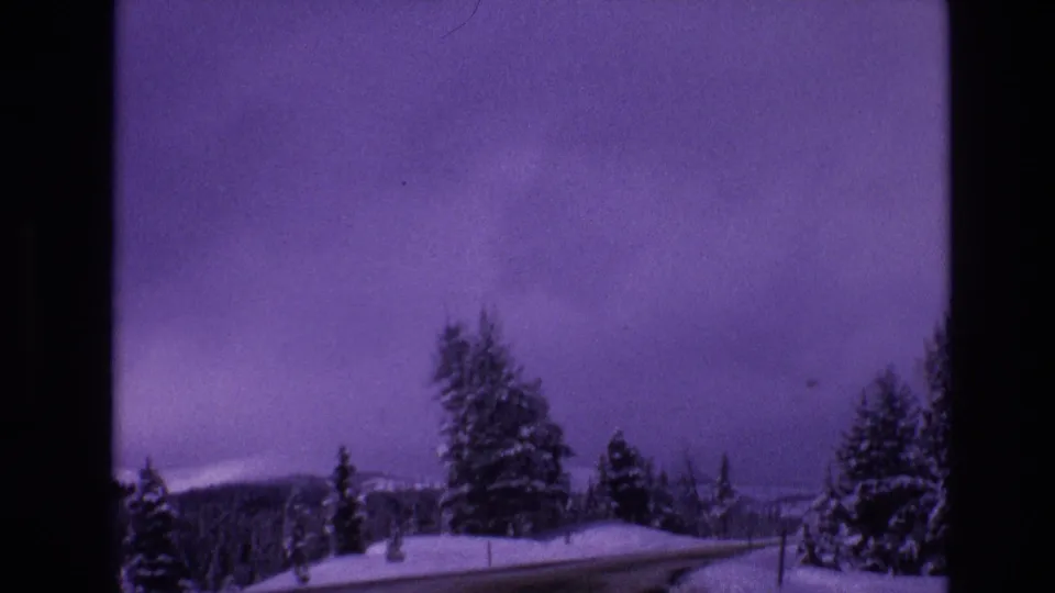 1974 Vail, Colorado frame with a curving snow-lined road, dark evergreen trees, distant mountain ridge, and visible 8mm color shift.