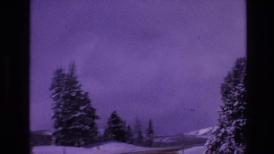 1974 Vail, Colorado 8mm frame showing a snowbound roadside, clustered conifers, distant mountain shapes, and strong purple film coloration.