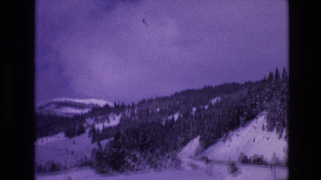 Vail, Colorado 1974 8mm frame showing a snowy evergreen-covered hillside with a road running along the mountain slope under an overcast sky.