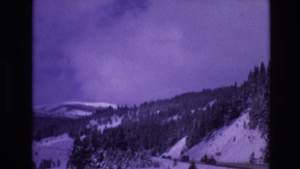Vail, Colorado 1974 8mm frame showing a snow-covered hillside, dark evergreen trees, and a curving road at the base of the slope.