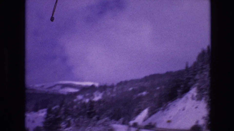 Vail, Colorado 1974 frame with motion-softened snowy hills, evergreen trees, and a road crossing the lower mountain slope.