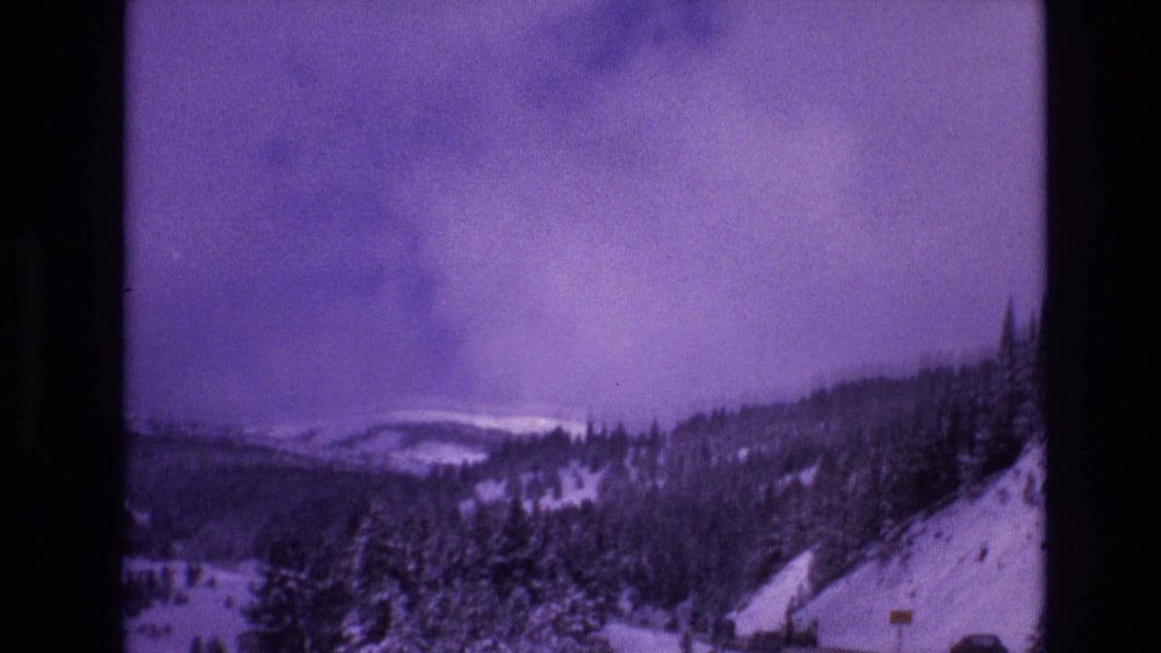 1974 8mm home-movie frame from Vail, Colorado showing snow-covered forest slopes and distant ridges beneath a heavy purple-tinged sky.