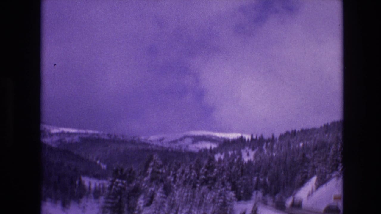1974 Vail, Colorado frame showing a winter mountain valley with snow-covered trees, distant ridgelines, and a purple cast from aged 8mm film.