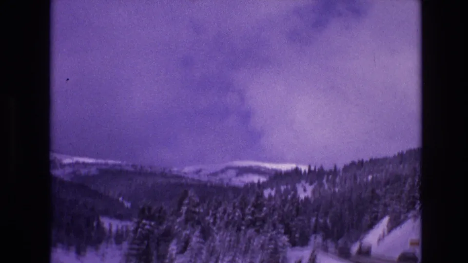 1974 Vail, Colorado frame showing a winter mountain valley with snow-covered trees, distant ridgelines, and a purple cast from aged 8mm film.