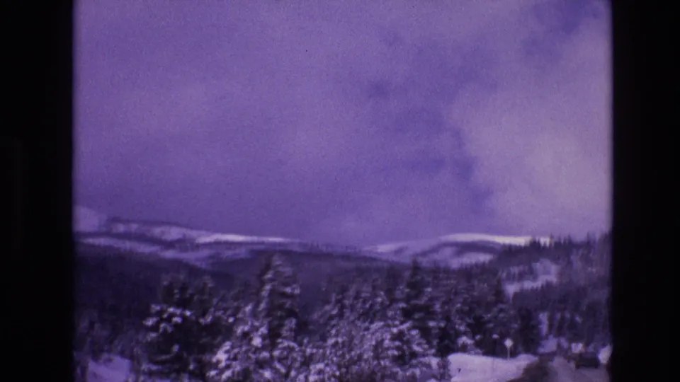Final 1974 Vail, Colorado home-movie frame showing snowy evergreens in the foreground, distant rounded mountain ridges, and a purple storm-cloud sky.