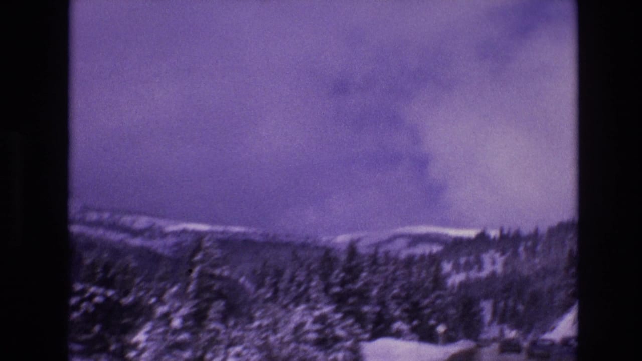 1974 Vail, Colorado home-movie frame showing snow-covered evergreens, mountain slopes, and a winter road glimpsed at the lower edge.