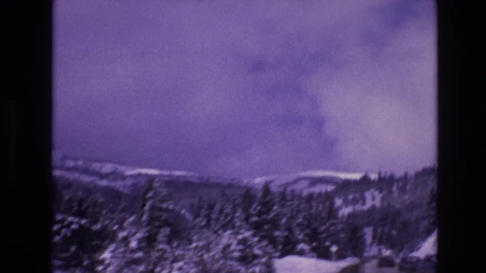 1974 Vail, Colorado home-movie frame showing snow-covered evergreens, mountain slopes, and a winter road glimpsed at the lower edge.