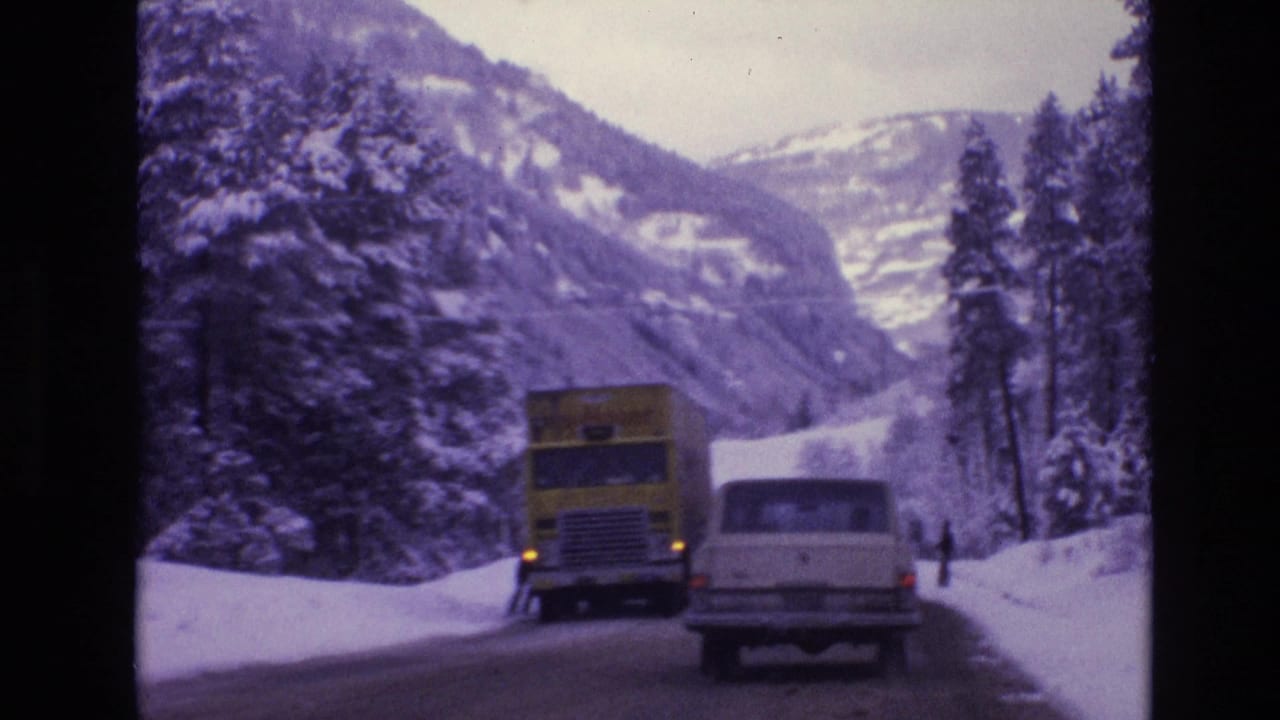 Yellow truck and white station wagon on a snow-banked mountain road.