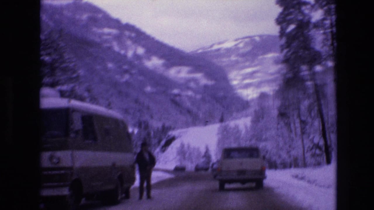 1974 Vail, Colorado 8mm frame showing a snowy mountain road with a camper van, a light pickup truck, a distant adult figure, pine trees, and snow-covered slopes.