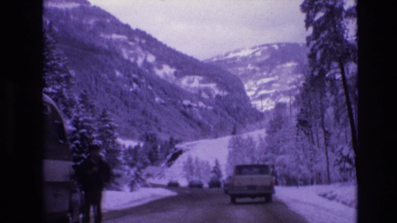 1974 Vail, Colorado 8mm frame looking along a snowy road toward forested mountains, with a pickup truck ahead and an adult figure near a partly visible camper van.