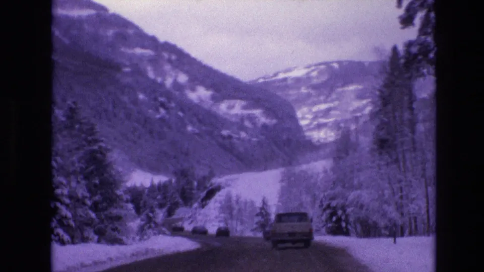 1974 Vail, Colorado 8mm frame of a pickup truck moving away along a snowy mountain road lined with trees and snowbanks.