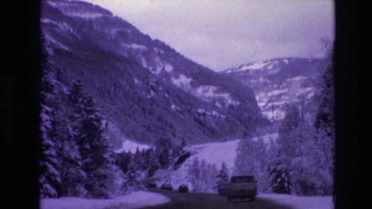 1974 Vail, Colorado 8mm frame showing a snow-lined mountain road with vehicles, evergreen trees, and steep winter slopes in the distance.