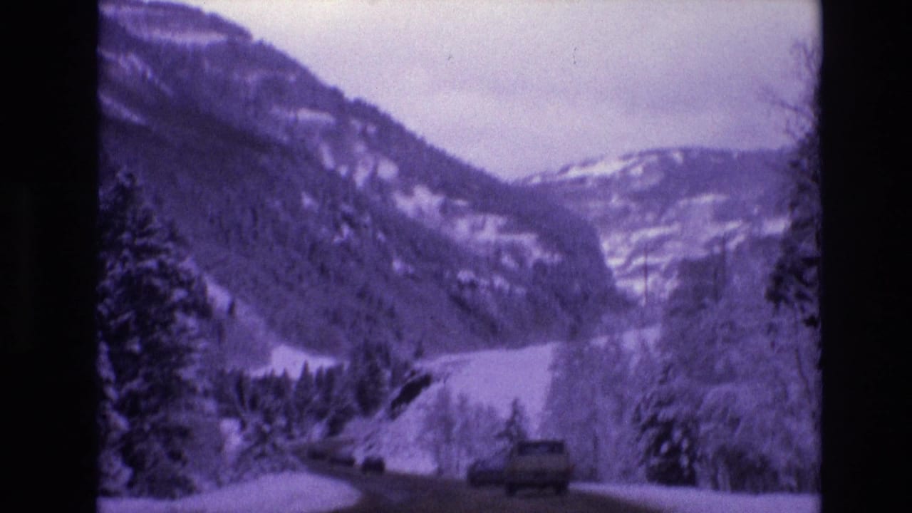 Vehicle traveling along a snow-covered road through a mountain valley.