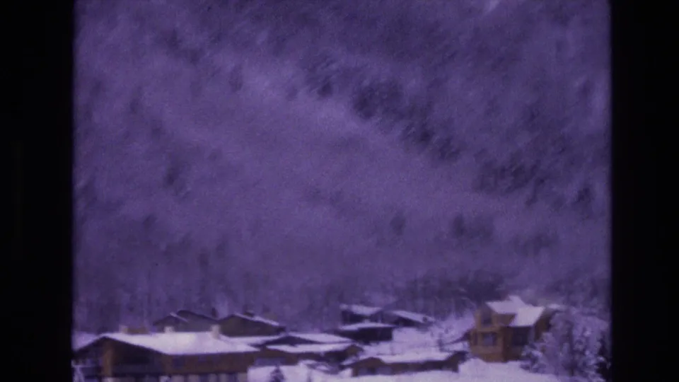 1974 Vail, Colorado 8mm frame showing lodge-like resort buildings below a snowy, tree-covered mountainside.