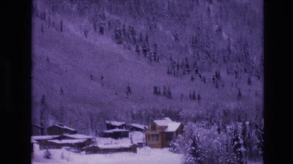 1974 Vail, Colorado frame with wooden lodge structures in the foreground and a wide snow-covered hillside rising behind them.