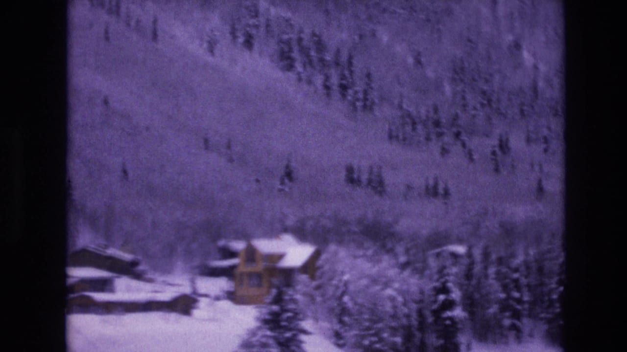 Cabins and trees in a snowy mountain landscape with dark film borders.