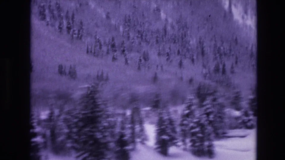1974 Vail, Colorado frame showing snow-covered evergreens and a wooded mountainside, with cabin structures partly visible near the lower right edge.