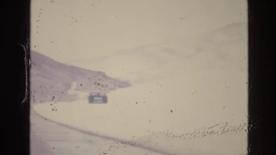 Soft, overexposed 8mm frame from the Vail, Colorado drive showing a snow-covered roadside, pale mountain shapes, and a small sign in the distance.