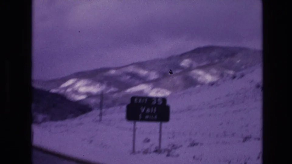 1974 Vail, Colorado 8mm frame showing a roadside sign reading Exit 35 Vail 1 Mile against snow-covered slopes and distant mountains.
