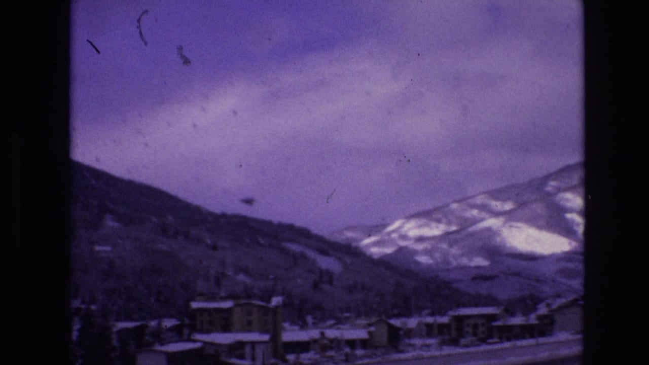 Snowy mountain town buildings below ridges and cloudy sky.