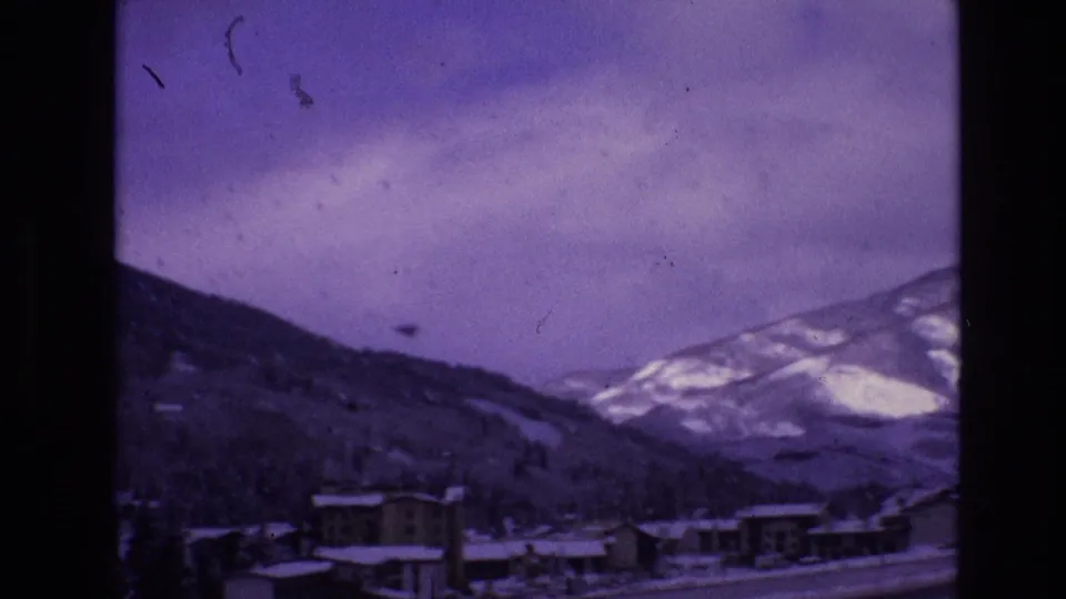Snow-dusted buildings in Vail, Colorado appear below mountain slopes in a purple-shifted 1974 8mm home-movie frame.