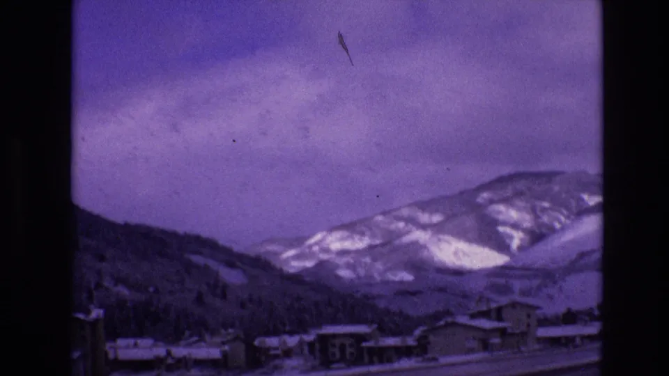 Final frame looking across a snowy Vail valley town toward mountain ridges under an overcast sky, with aged 8mm color shift visible.