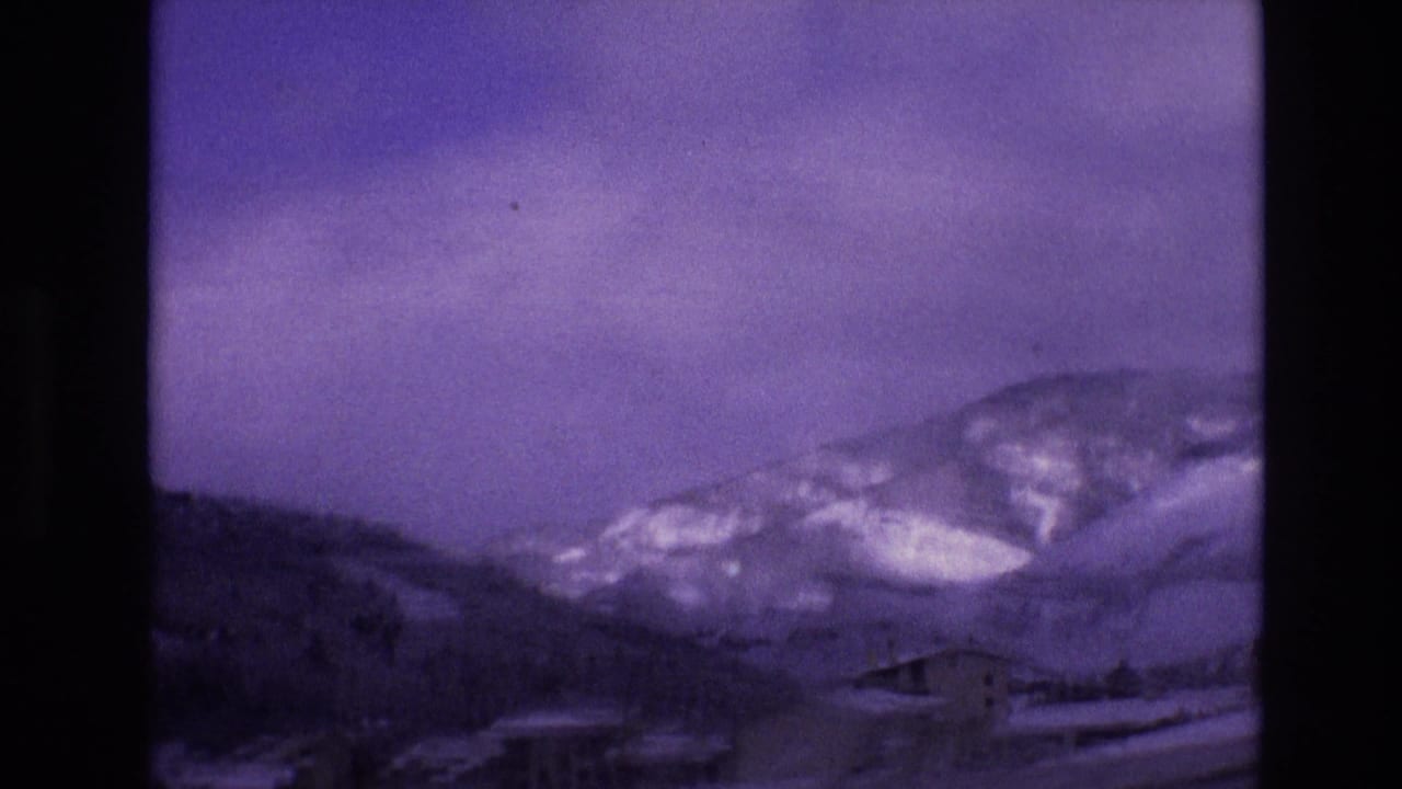 Snowy roadside view with lodge-like building and mountain slope beyond.