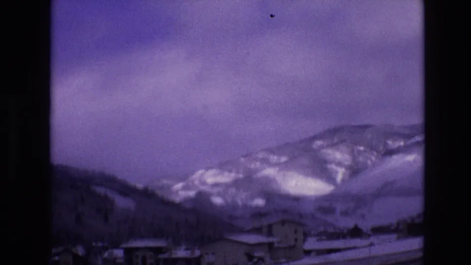 Soft 8mm frame from Vail, Colorado in 1974 showing a snow-covered valley town beneath broad winter mountain slopes and a purple cast from the film stock.
