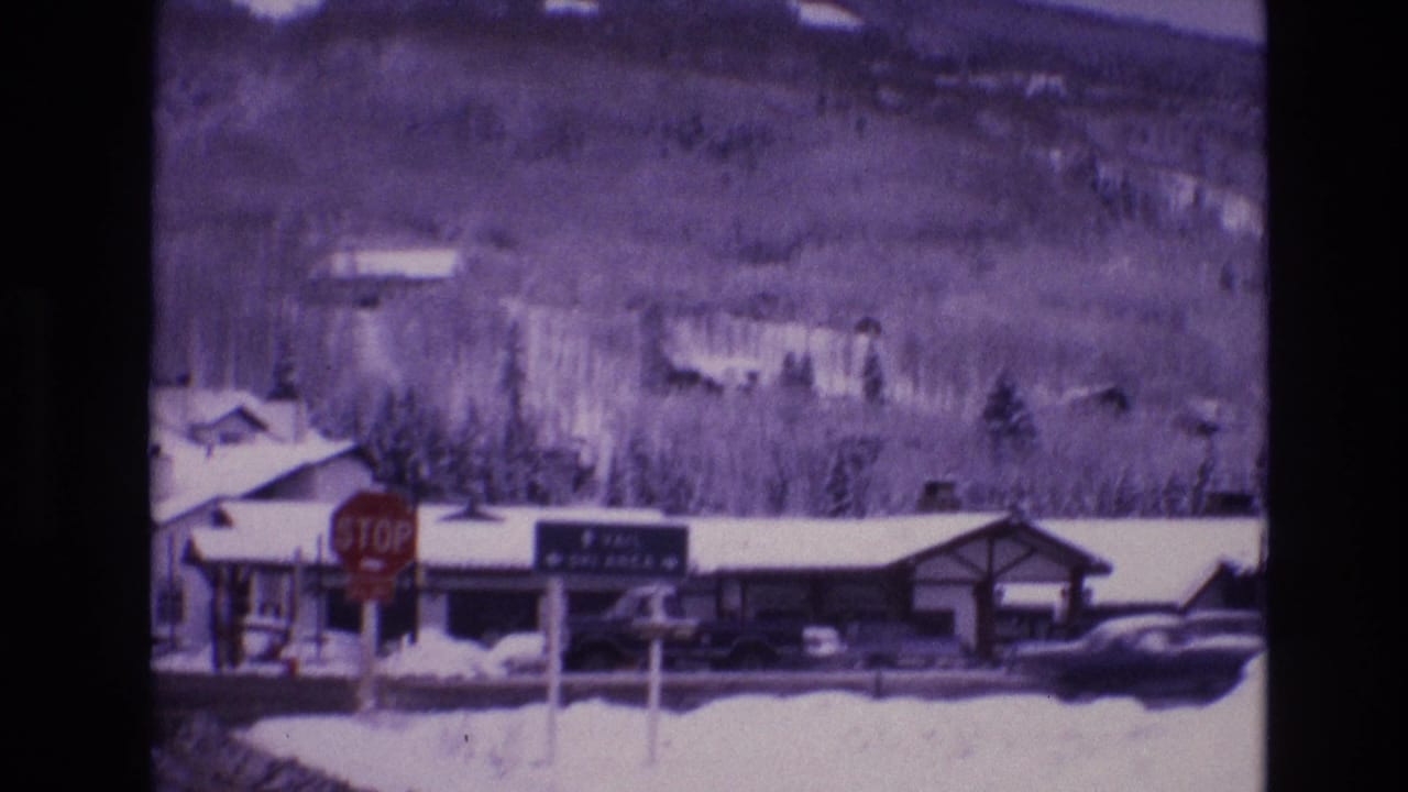 Stop sign and Vail Ski Area directional sign beside a snowy road and mountain-town buildings.