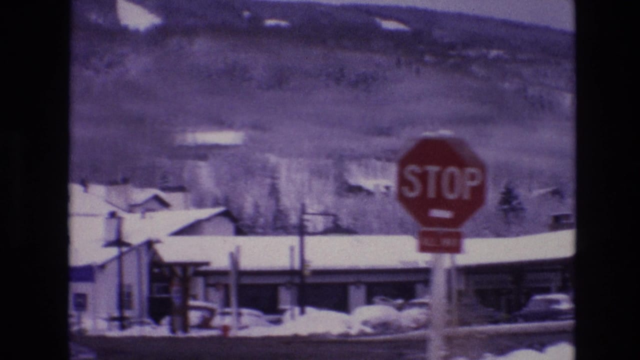 1974 Vail, Colorado street view with a red stop sign, snow-covered rooftops, parked cars, and wooded mountain slopes in the background.