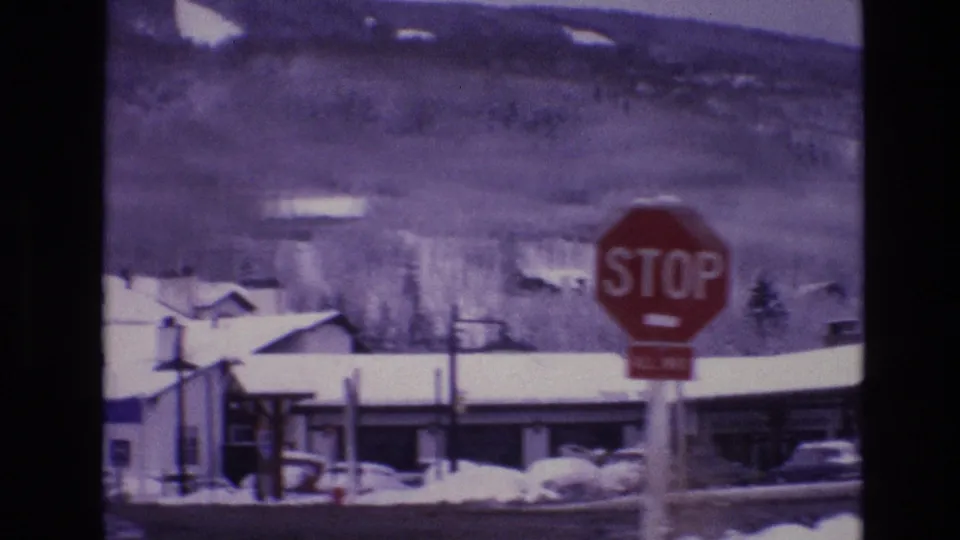 1974 Vail, Colorado street view with a red stop sign, snow-covered rooftops, parked cars, and wooded mountain slopes in the background.
