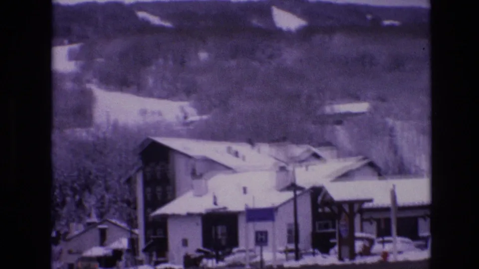 Snowy Vail, Colorado buildings and roadside structures appear below tree-covered mountain slopes in this 1974 home-movie frame.