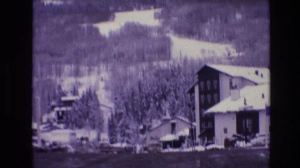 A 1974 Vail, Colorado view shows chalet-like buildings, snowbanks, evergreens, and a wooded mountain slope with bright snow patches above town.