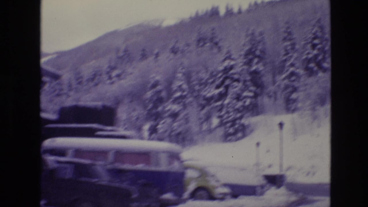 1974 Vail, Colorado 8mm frame showing a snow-covered road edge with parked cars, evergreen trees, and a wooded mountain slope in winter.