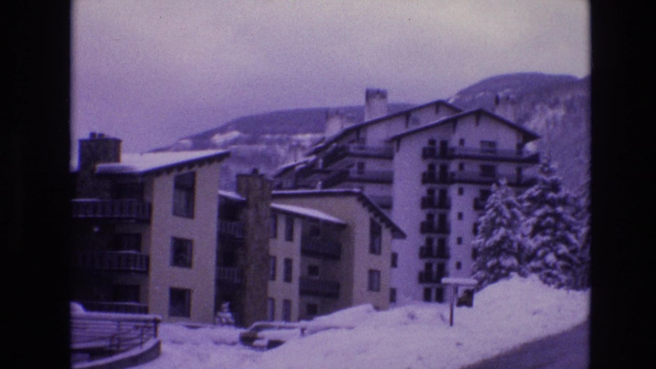 1974 Vail, Colorado 8mm frame showing multi-story apartment buildings with balconies, snow-covered roofs, parked cars, and a wooded mountain backdrop.