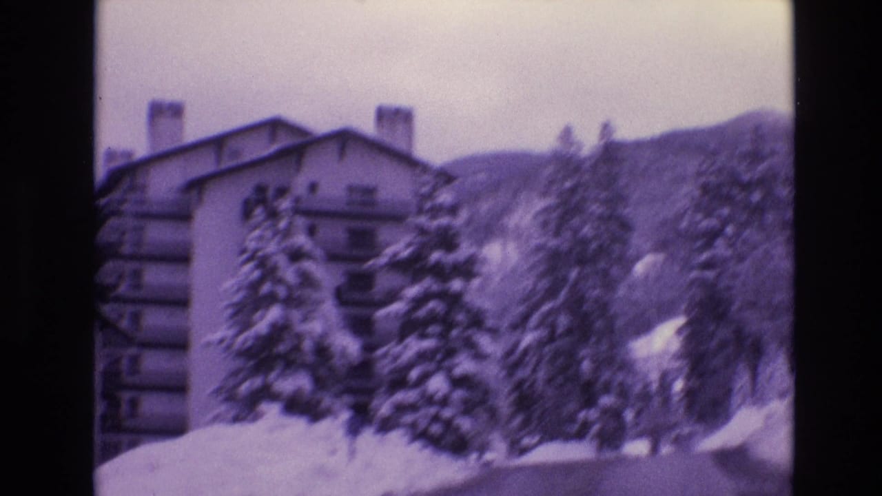 1974 Vail, Colorado home-movie frame showing a multi-story resort building partly obscured by snow-laden pine trees and a mountain slope.