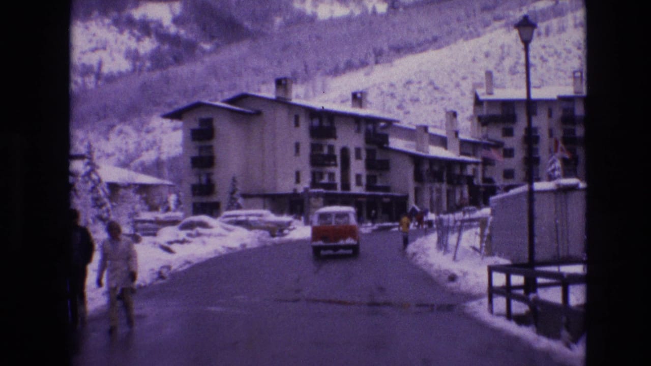 Red van drives along a snow-lined road past pedestrians and apartment buildings.