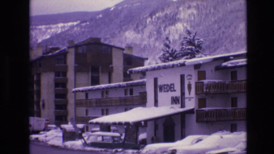 1974 Vail, Colorado frame of the Wedel Inn exterior, with snow on the roof and ground, parked cars, balcony railings, and wooded mountain slopes beyond.