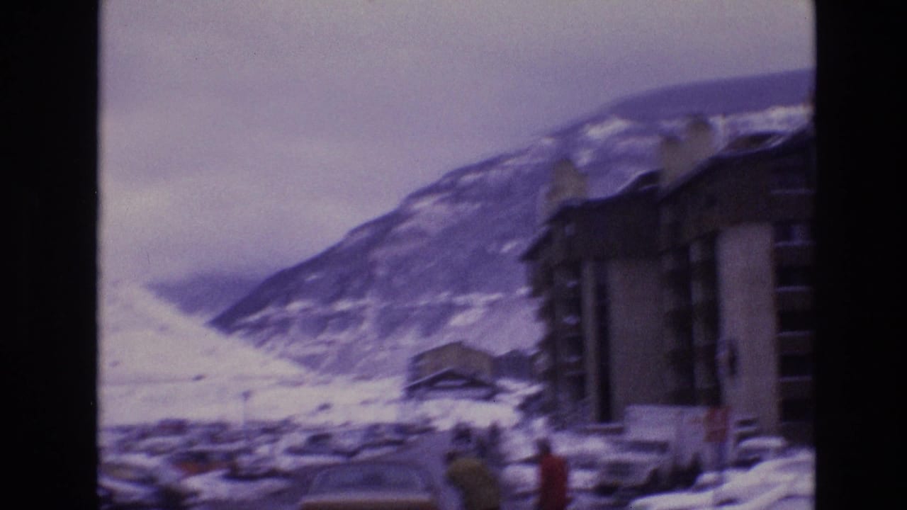 1974 Vail, Colorado home-movie frame showing snow-covered mountain slopes, lodge-style buildings, and a road viewed through soft purple-tinted 8mm film.