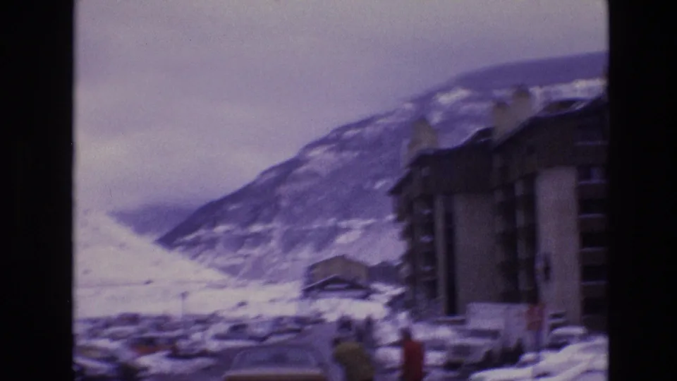 1974 Vail, Colorado home-movie frame showing snow-covered mountain slopes, lodge-style buildings, and a road viewed through soft purple-tinted 8mm film.