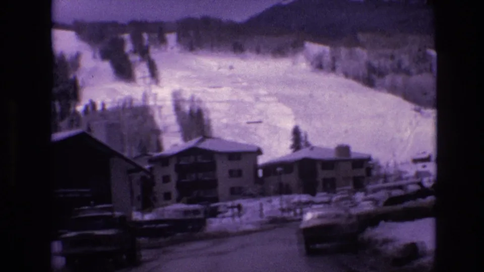 1974 Vail, Colorado frame showing a winter road, parked cars, lodge-style buildings, and snow-covered ski terrain under a purple-tinted 8mm home-movie look.