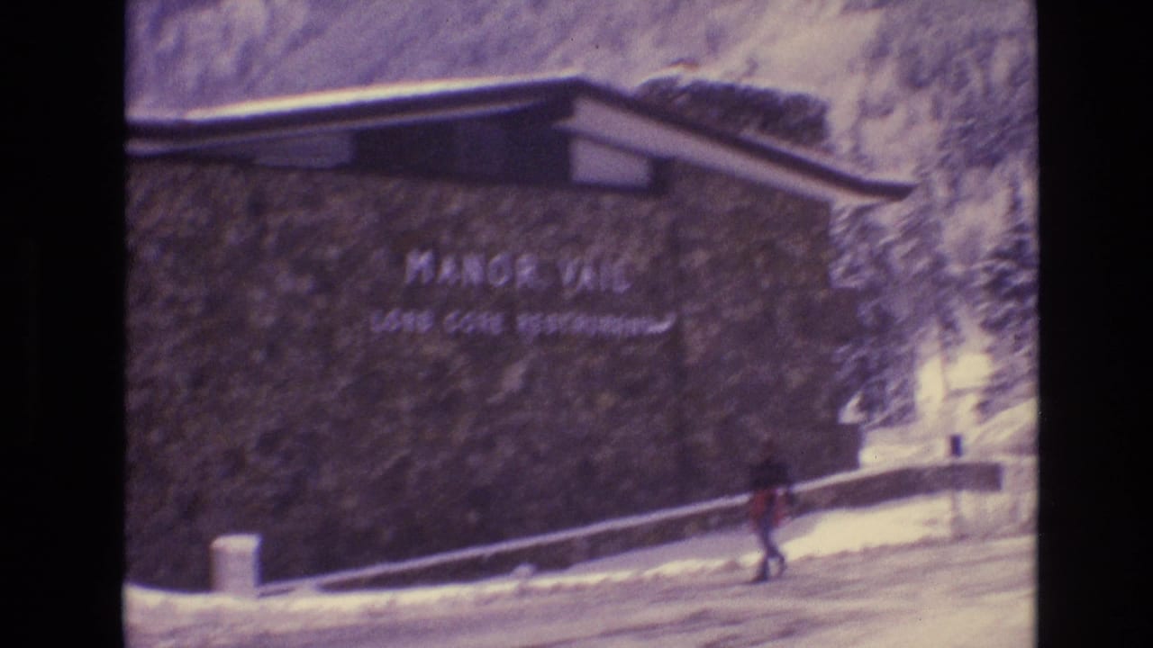 Stone lodge wall with Manor Vail Lodge sign and a person walking past in snow.