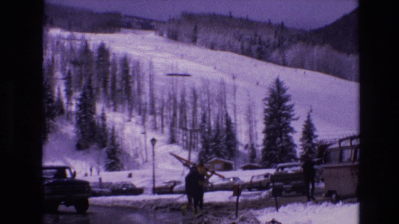 Person carrying skis near parked vehicles at a snowy ski area.